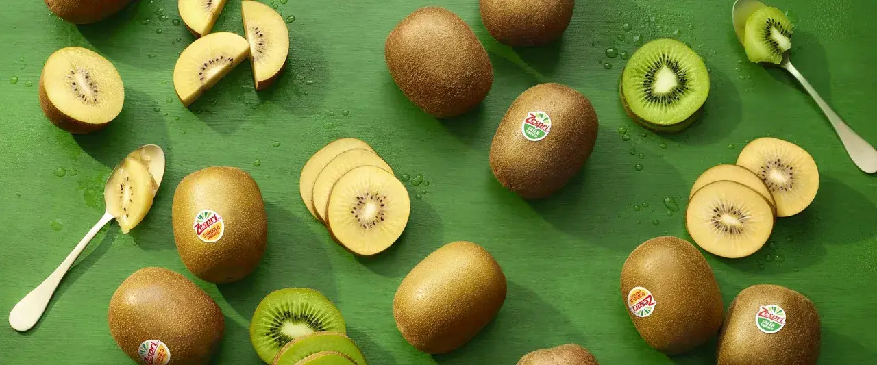 Gold- und grüne Kiwis, ganz und geschnitten, auf grünem Hintergrund. Ein Löffel mit Kiwi-Fruchtfleisch. Kiwi gesund und lecker.