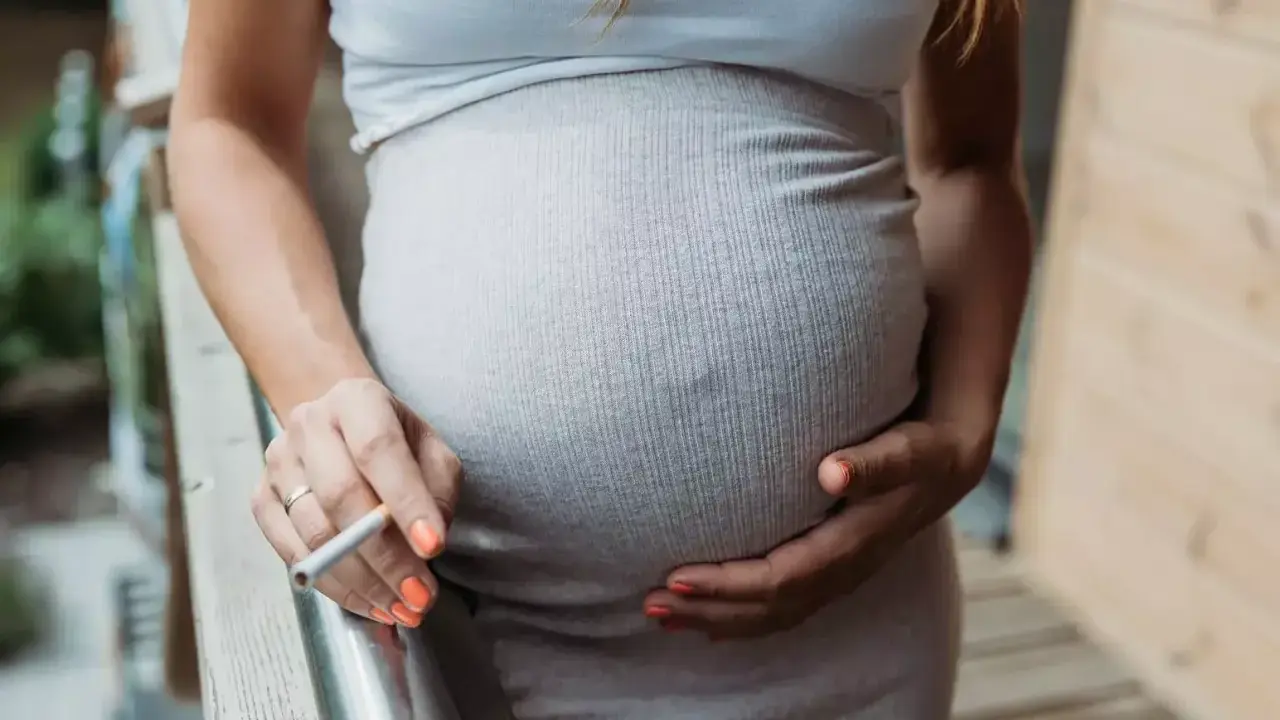 Schwanger, rauchen und stillen sind keine gute Kombination. Eine Frau hält eine Zigarette in der Hand, während sie ihren Bauch streichelt.