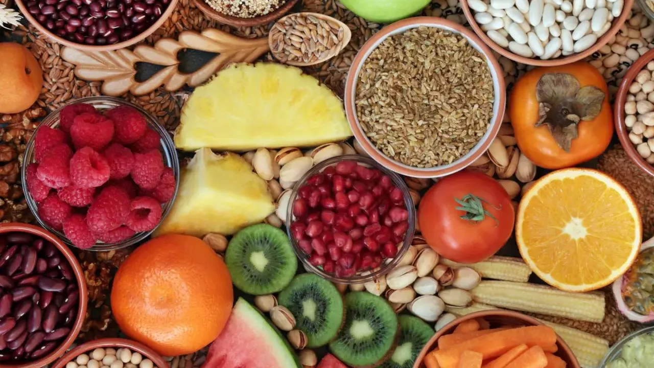 Vielfalt an ballaststoffreichen Lebensmitteln: Bohnen, Quinoa, Beeren, Obst, Gemüse und Nüsse für eine gesunde Ernährung.