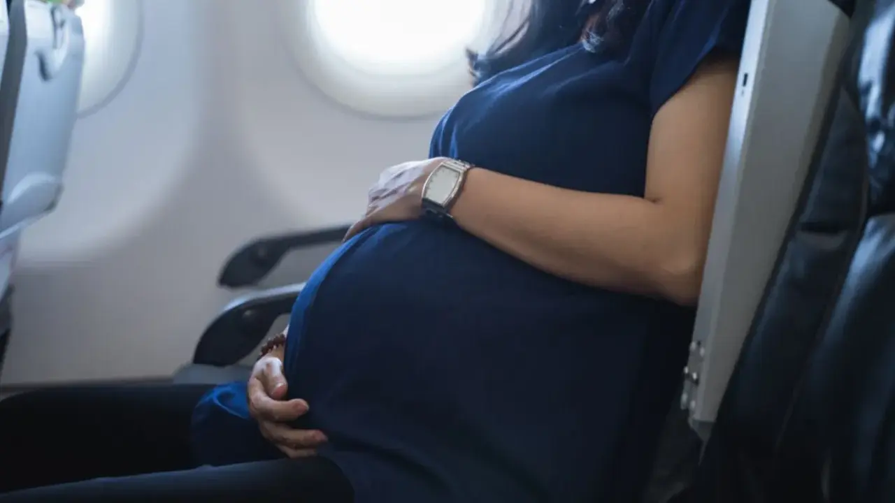 Eine schwangere Frau sitzt im Flugzeug und hält ihren Bauch. Sie fliegt entspannt in den Urlaub.