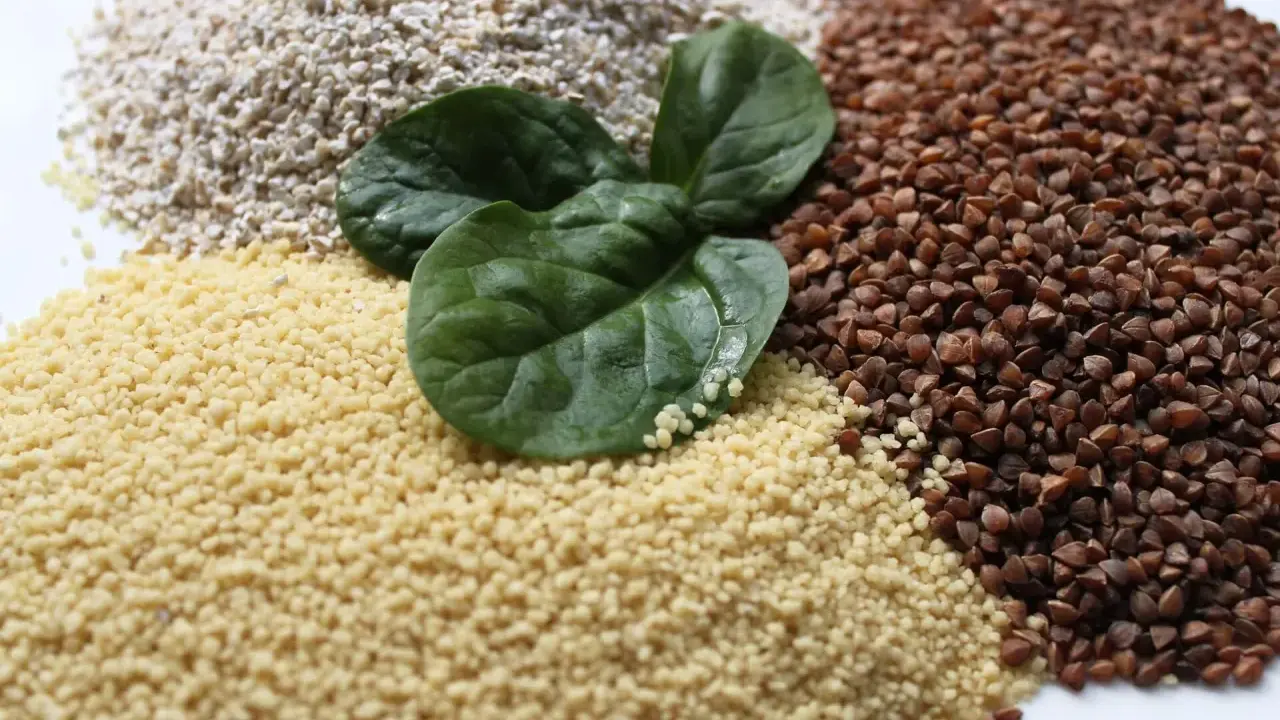 Haufen von Couscous, Buchweizen und Haferflocken, garniert mit frischen Spinatblättern. Ist Couscous gesund? Ja, es ist eine gute Quelle für Ballaststoffe.