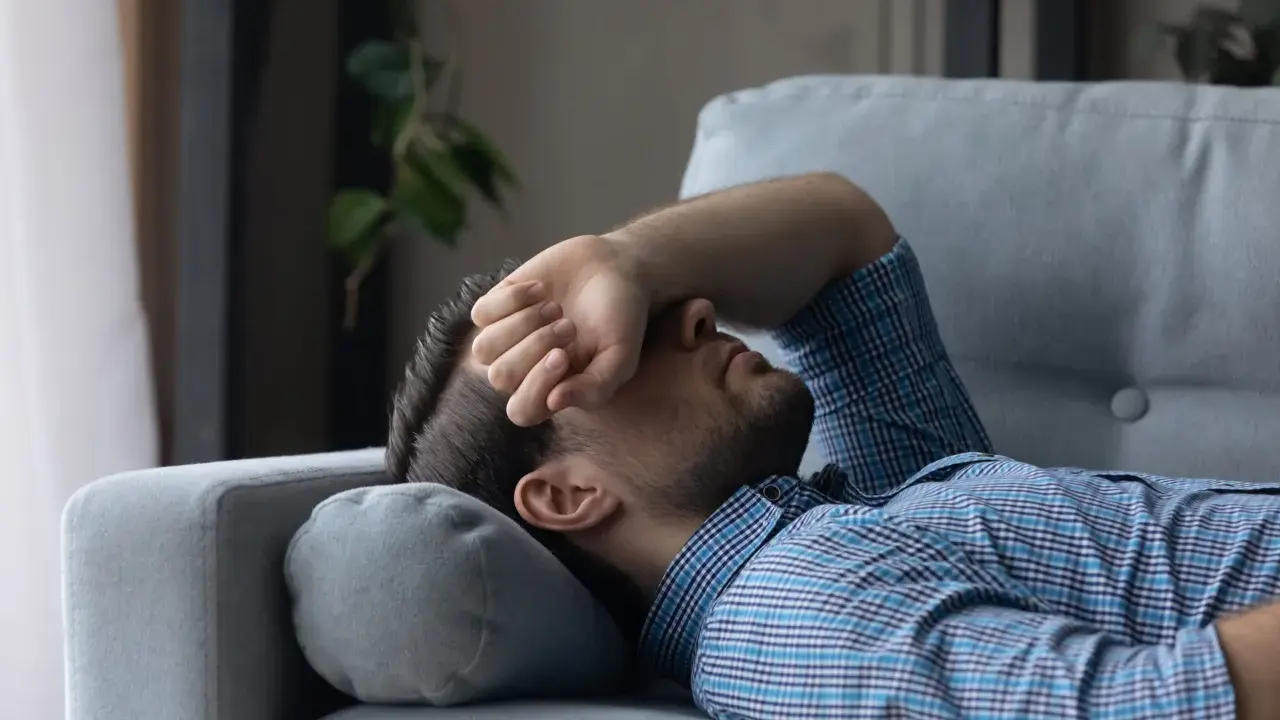 Mann liegt erschöpft auf Sofa, Hand vor dem Gesicht. Er sucht nach Tipps, wie man nach Koks schlafen kann, um endlich Ruhe zu finden.