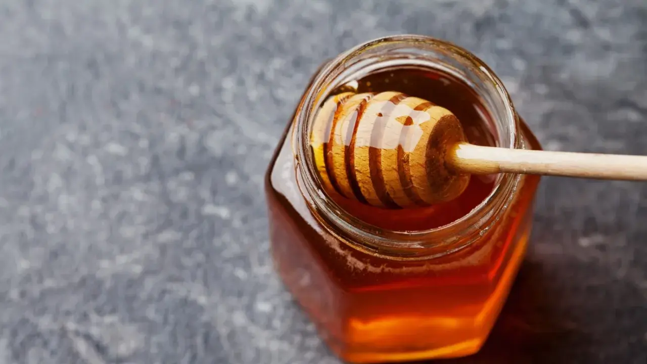 Ein Glas mit flüssigem Honig und einem Honigheber. Dieser goldene Nektar ist nicht nur lecker, sondern auch honig gesund.