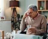 Ein Mann im Rollstuhl hält ein Glas Wasser, die Hand an der Stirn. Ein Bild, das den **Parkinson Verlauf nach 10 Jahren** symbolisiert, mit Müdigkeit und Sorge.