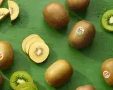 Gold- und grüne Kiwis, ganz und geschnitten, auf grünem Hintergrund. Ein Löffel mit Kiwi-Fruchtfleisch. Kiwi gesund und lecker.
