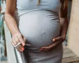 Schwanger, rauchen und stillen sind keine gute Kombination. Eine Frau hält eine Zigarette in der Hand, während sie ihren Bauch streichelt.