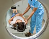 Eine Patientin liegt für eine MRT Untersuchung auf einer Liege, während eine medizinische Fachkraft sie vorbereitet.