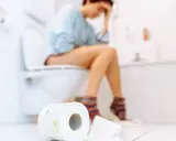 Frau sitzt auf Toilette, fühlt sich unwohl. Durchfall in der Schwangerschaft ist belastend. Toilettenpapier liegt bereit.