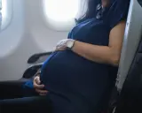 Eine schwangere Frau sitzt im Flugzeug und hält ihren Bauch. Sie fliegt entspannt in den Urlaub.