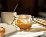 Glas mit cremiger Erdnussbutter, die gesund und lecker ist. Daneben ein Stück Toast.