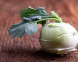 Ein frischer Kohlrabi mit grünen Blättern liegt auf einem rustikalen Holztisch. Kohlrabi gesund und vielseitig.