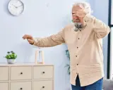 Älterer Mann mit weißem Haar und Bart hält sich die Augen zu, als hätte er Schwindel nach dem Aufstehen. Er tastet unsicher nach vorne.