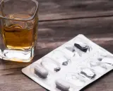 Ein Glas mit bernsteinfarbener Flüssigkeit und eine Blisterpackung mit einigen verbleibenden Pillen. Die Kombination von paracetamol und alkohol kann gefährlich sein.