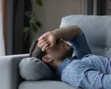 Mann liegt erschöpft auf Sofa, Hand vor dem Gesicht. Er sucht nach Tipps, wie man nach Koks schlafen kann, um endlich Ruhe zu finden.
