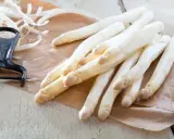 Frischer weißer Spargel liegt auf braunem Papier, daneben ein Sparschäler. Die Frage, warum riecht Urin nach Spargel, beschäftigt viele.