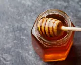 Ein Glas mit flüssigem Honig und einem Honigheber. Dieser goldene Nektar ist nicht nur lecker, sondern auch honig gesund.