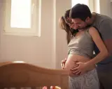 Ein Mann umarmt seine schwangere Frau, die ihren Bauch streichelt. Sie warten gespannt auf ihr Baby. Senkwehen ab wann?