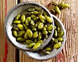 Grüne Pistazienkerne in zwei Schalen auf Holzuntergrund. Diese gesunden Pistazien sind ein leckerer Snack.