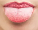 Nahaufnahme einer Zunge mit einem leichten, rosafarbenen belag auf der zunge. Die Lippen sind leicht geöffnet.