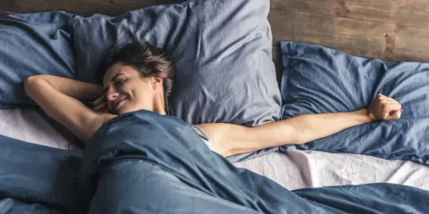 Frau streckt sich im Bett. Wenn man nicht schlafen kann, hilft es manchmal, sich zu bewegen.