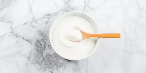 Weißes Kollagenpulver in einer Schale mit Holzlöffel. Die Wirkung von Kollagen für Haut und Gelenke wird oft diskutiert.