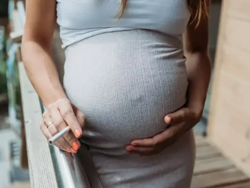 Schwanger, rauchen und stillen sind keine gute Kombination. Eine Frau hält eine Zigarette in der Hand, während sie ihren Bauch streichelt.