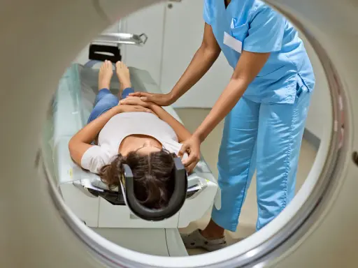 Eine Patientin liegt für eine MRT Untersuchung auf einer Liege, während eine medizinische Fachkraft sie vorbereitet.