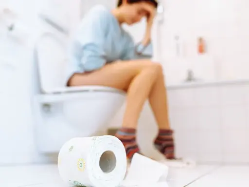 Frau sitzt auf Toilette, fühlt sich unwohl. Durchfall in der Schwangerschaft ist belastend. Toilettenpapier liegt bereit.