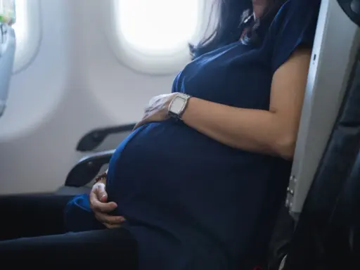 Eine schwangere Frau sitzt im Flugzeug und hält ihren Bauch. Sie fliegt entspannt in den Urlaub.