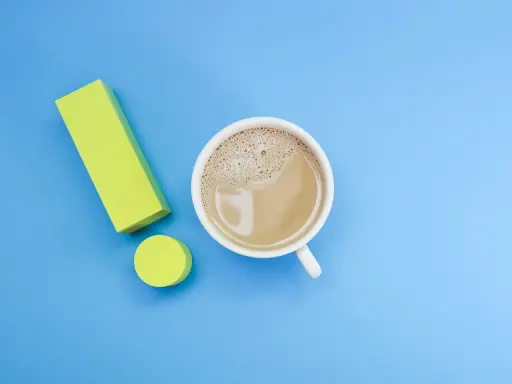 Ein Ausrufezeichen aus gelben Blöcken neben einer Tasse Kaffee. Ein starker Kaffee für einen energiegeladenen Tag, vielleicht mit einem Hauch von Lithium für extra Power.