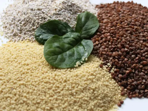 Haufen von Couscous, Buchweizen und Haferflocken, garniert mit frischen Spinatblättern. Ist Couscous gesund? Ja, es ist eine gute Quelle für Ballaststoffe.