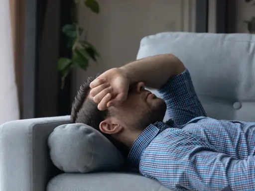 Mann liegt erschöpft auf Sofa, Hand vor dem Gesicht. Er sucht nach Tipps, wie man nach Koks schlafen kann, um endlich Ruhe zu finden.