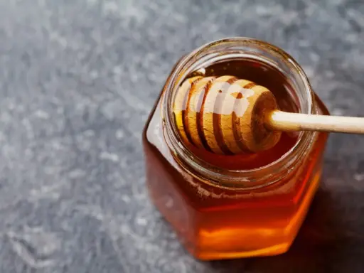 Ein Glas mit flüssigem Honig und einem Honigheber. Dieser goldene Nektar ist nicht nur lecker, sondern auch honig gesund.