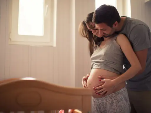 Ein Mann umarmt seine schwangere Frau, die ihren Bauch streichelt. Sie warten gespannt auf ihr Baby. Senkwehen ab wann?