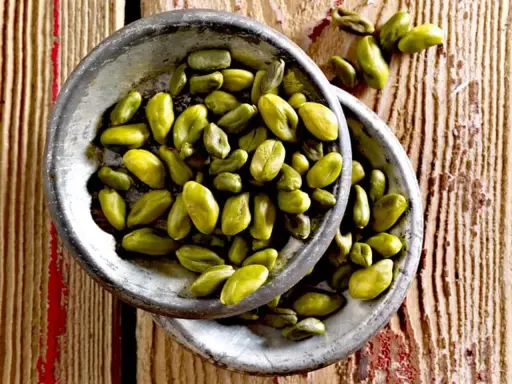 Grüne Pistazienkerne in zwei Schalen auf Holzuntergrund. Diese gesunden Pistazien sind ein leckerer Snack.