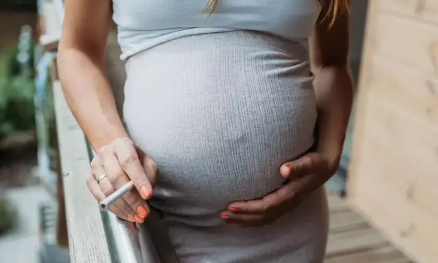 Schwanger, rauchen und stillen sind keine gute Kombination. Eine Frau hält eine Zigarette in der Hand, während sie ihren Bauch streichelt.
