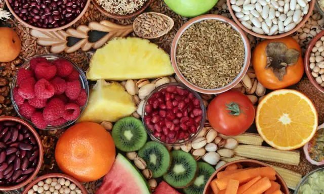 Vielfalt an ballaststoffreichen Lebensmitteln: Bohnen, Quinoa, Beeren, Obst, Gemüse und Nüsse für eine gesunde Ernährung.