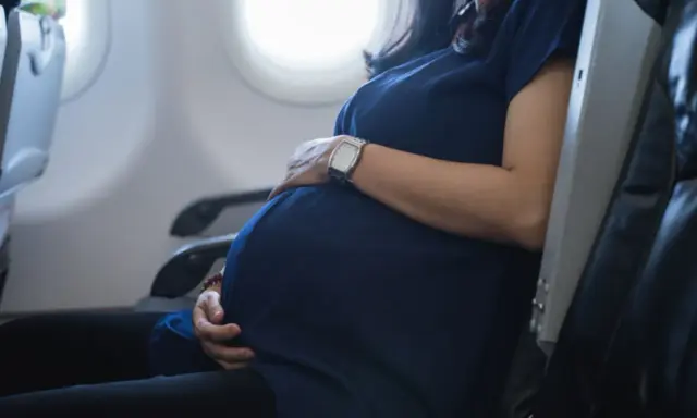 Eine schwangere Frau sitzt im Flugzeug und hält ihren Bauch. Sie fliegt entspannt in den Urlaub.
