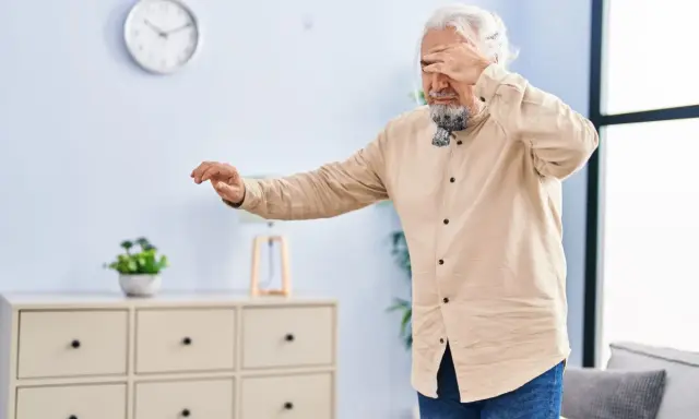 Älterer Mann mit weißem Haar und Bart hält sich die Augen zu, als hätte er Schwindel nach dem Aufstehen. Er tastet unsicher nach vorne.