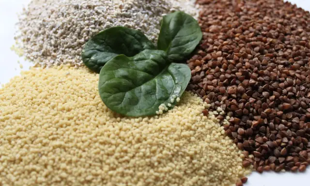 Haufen von Couscous, Buchweizen und Haferflocken, garniert mit frischen Spinatblättern. Ist Couscous gesund? Ja, es ist eine gute Quelle für Ballaststoffe.
