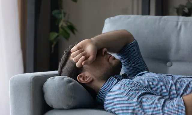 Mann liegt erschöpft auf Sofa, Hand vor dem Gesicht. Er sucht nach Tipps, wie man nach Koks schlafen kann, um endlich Ruhe zu finden.