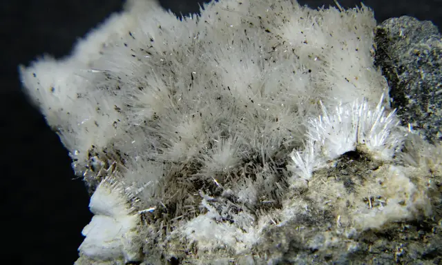 Feine, nadelartige Kristalle von Mesolith, einem Zeolith, wachsen aus einem grauen Gestein. Die Zeolith Wirkung ist faszinierend.