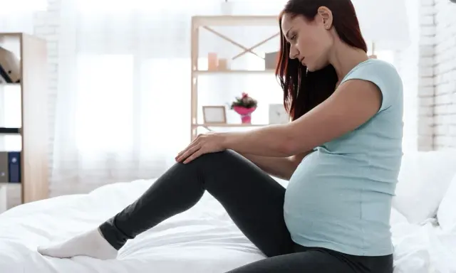 Schwangere Frau mit unruhigen Beinen, die auf einem Bett sitzt und ihr Bein berührt.