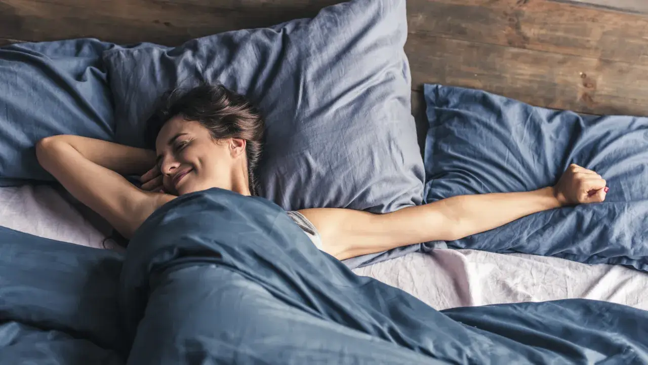 Frau streckt sich im Bett. Wenn man nicht schlafen kann, hilft es manchmal, sich zu bewegen.