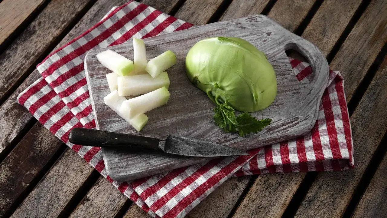Ein ganzer und geschnittener Kohlrabi liegen auf einem Holzbrett, daneben ein Messer und eine karierte Serviette. Kohlrabi gesund und lecker!