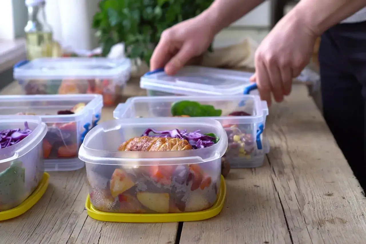 Vorbereitung von Mahlzeiten: Mehrere Behälter mit Hähnchen, Gemüse und Bohnen werden für das Meal Prep auf einem Holztisch arrangiert.