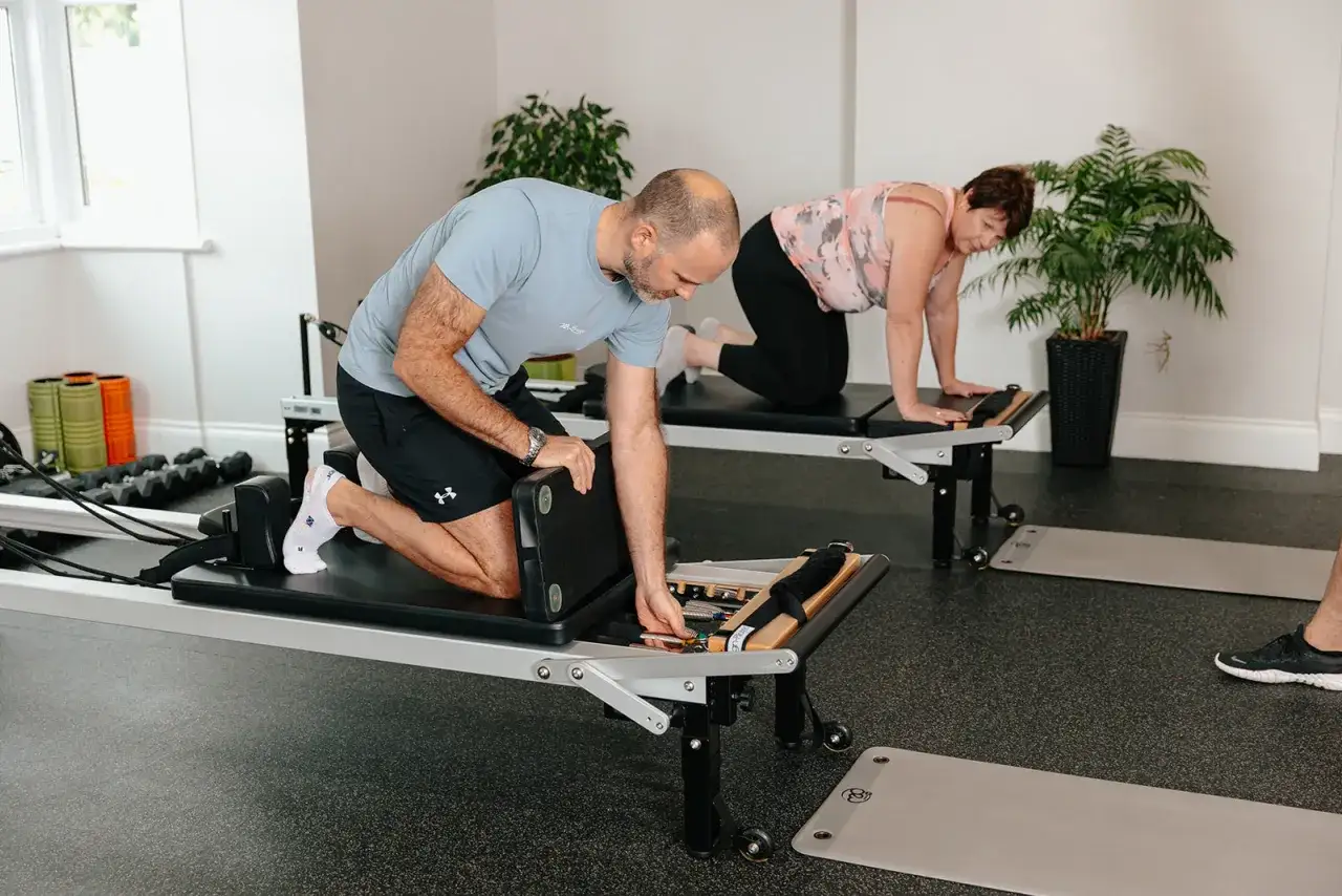 Mann und Frau trainieren auf Reformer Pilates Geräten.