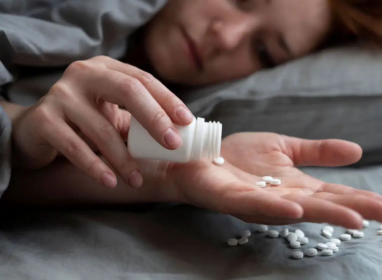 Eine Person nimmt Tabletten aus einer Flasche in ihre Hand. Es scheint, als ob sie Amitriptylin zum Schlafen einnimmt, um Ruhe zu finden.