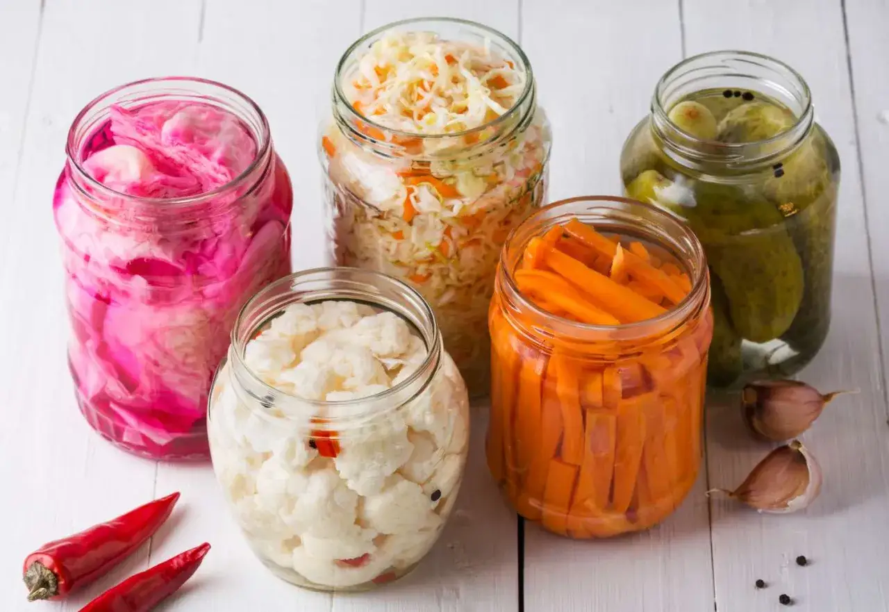 F&uuml;nf Gl&auml;ser mit fermentierten Lebensmitteln: Rotkohl, Sauerkraut, Blumenkohl, Karotten und Gew&uuml;rzgurken.