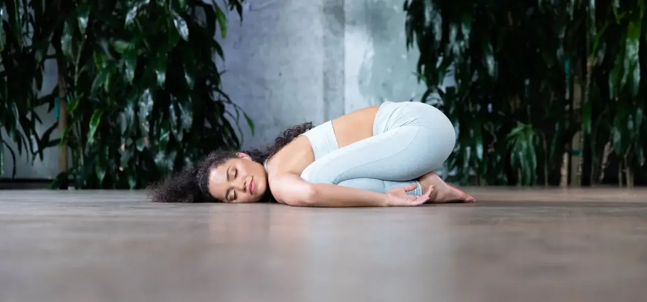 Frau in Kindhaltung auf dem Boden, entspannt. Eine sanfte Yoga-Pose, die bei PMS hilft und Ruhe bringt.